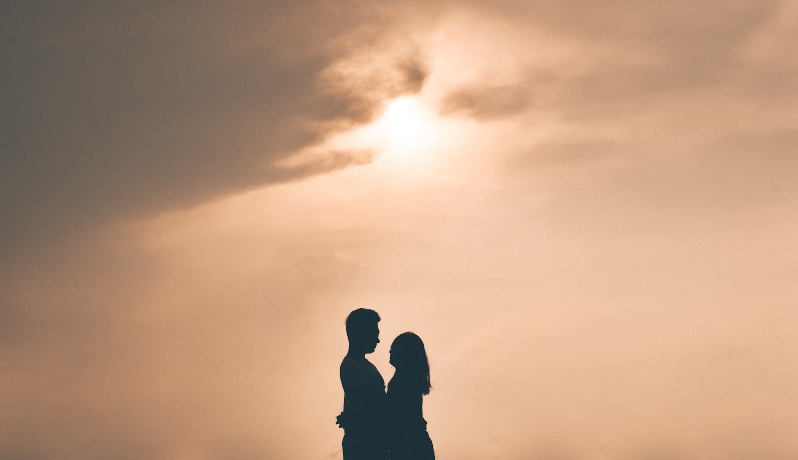 Two silhouetted figures embracing on a beach at dusk