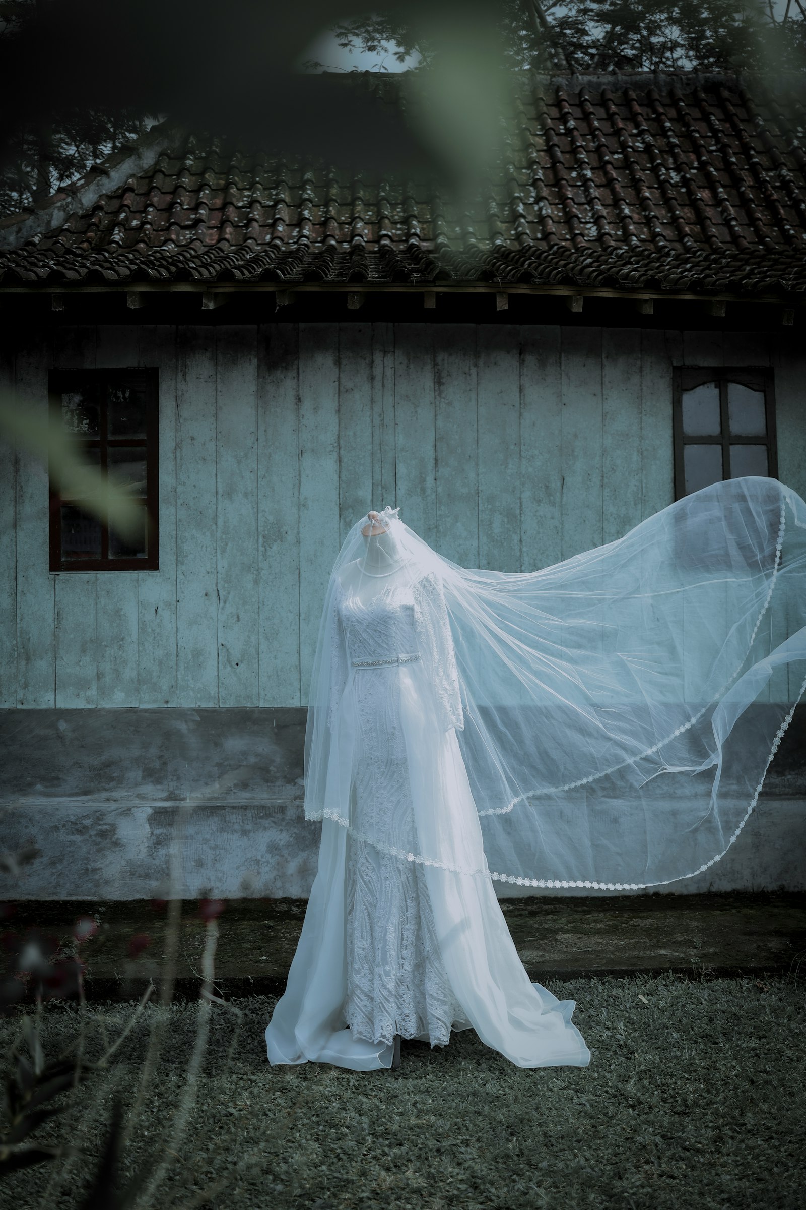 A bride in a dark, dramatic wedding dress and veil standing in a shadowy interior