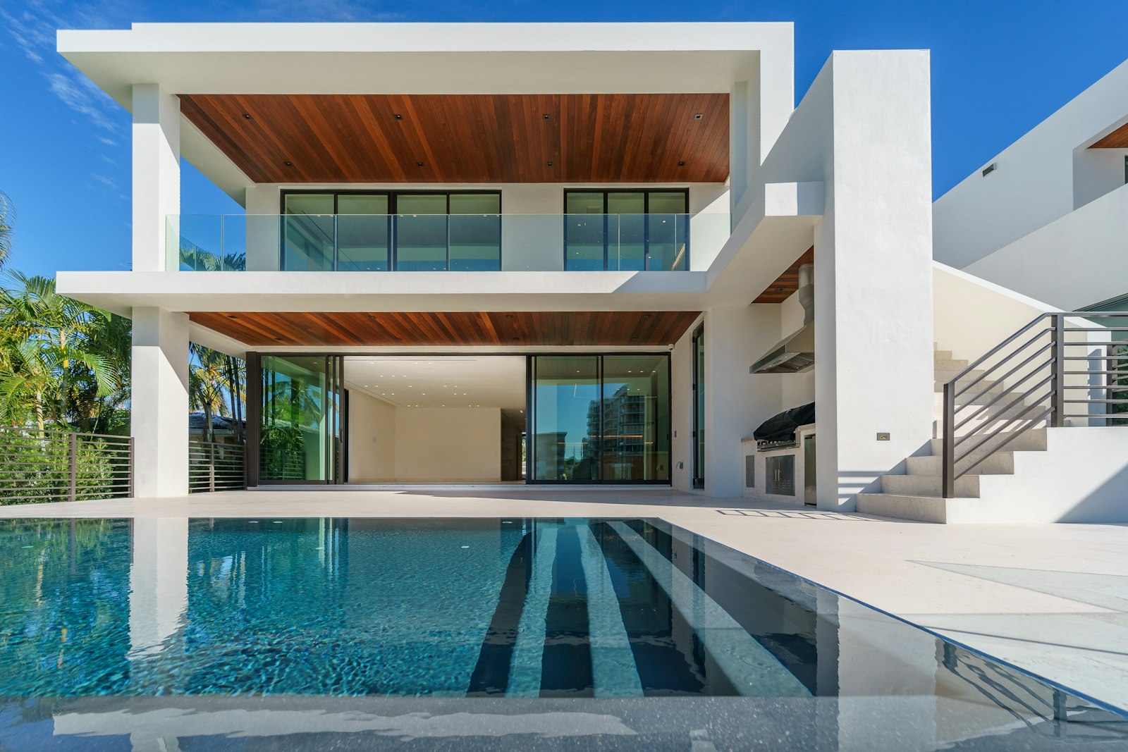 A modern villa with an infinity pool under blue sky, wood-soffit terraces stepping toward the water
