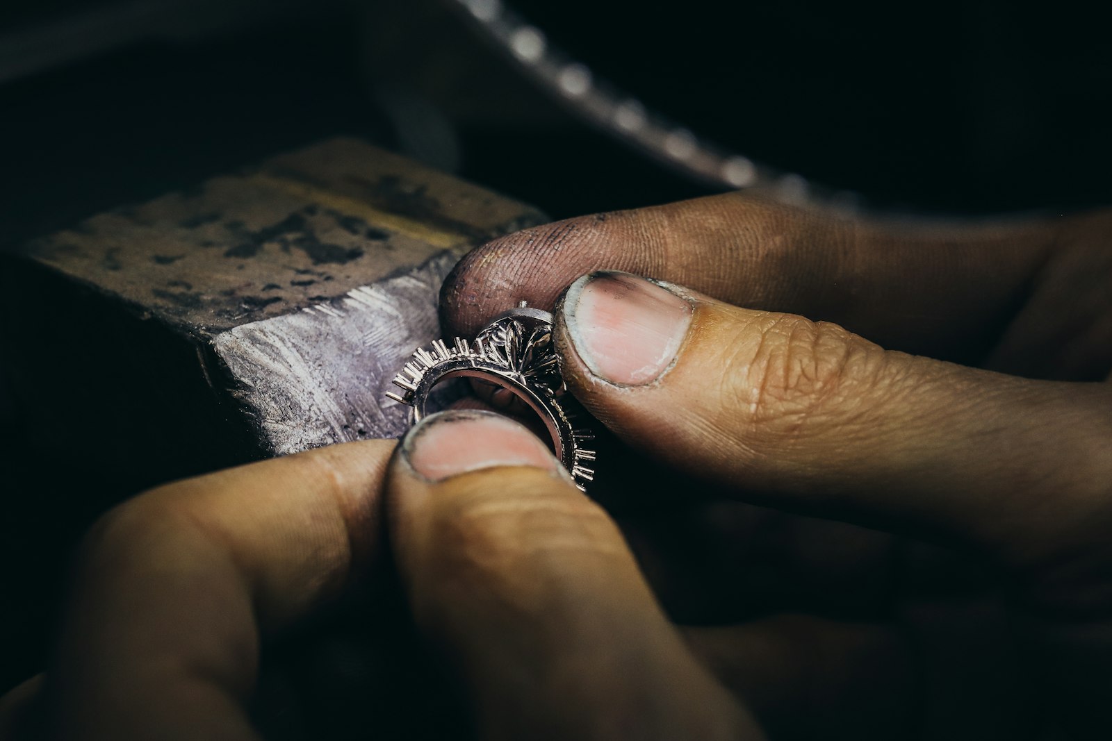 Close-up of a jeweller's hands setting a diamond into a ring under focused light at the bench.